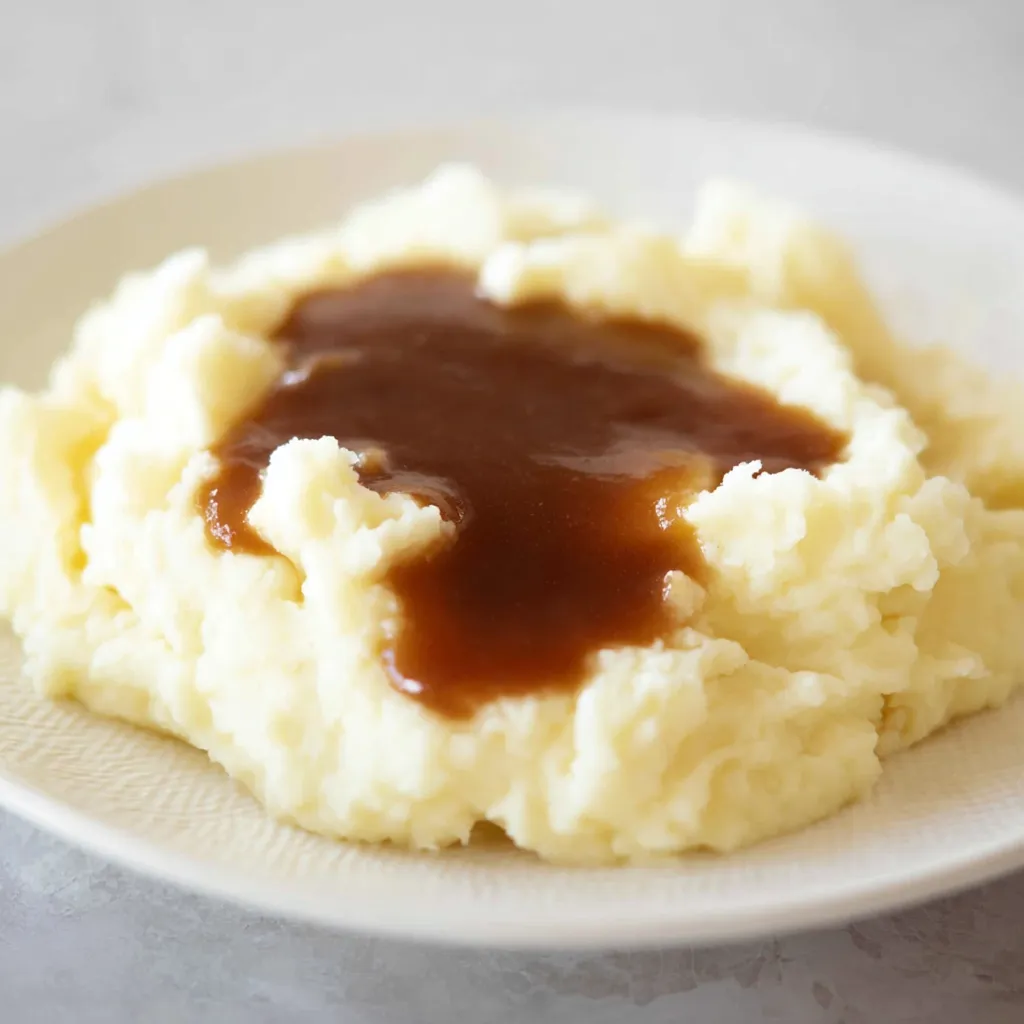 A close-up of fluffy white mashed potatoes with a rich, dark brown gravy pooled in the center, on a white plate.