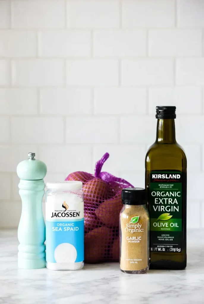 A light blue pepper grinder, Jacobsen salt container, purple bag of organic red potatoes, garlic powder, and olive oil bottle.